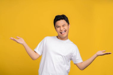 Beyaz tişört giyen Asyalı adam sarı stüdyo arka planında fotokopi alanı olan bir şey için heyecanlıydı..