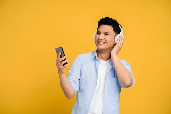 スマートフォンやワイヤレスヘッドフォンを使用してハンサムな若いアジア人 彼は電話で音楽を聞く — ストック写真