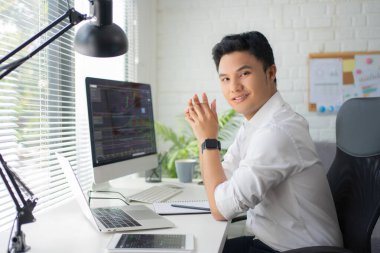 Yakışıklı Asyalı iş adamı masasındaki dizüstü bilgisayarında hisse senedi ticareti yapıyor. Veri analiz kavramı.