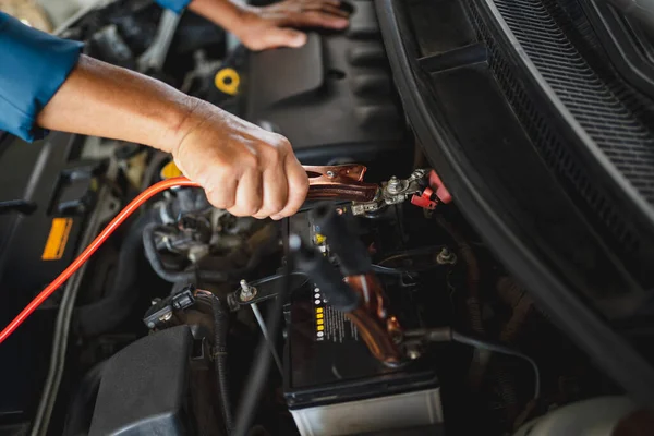 Car mechanic uses a battery jumper cable to charge the dead battery. Car repair service concept.