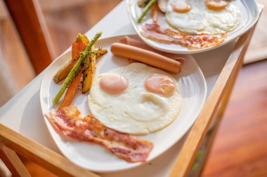 Beyaz bir tabakta kızarmış yumurta, sosis, domuz pastırması ve sebzelerle kahvaltı..