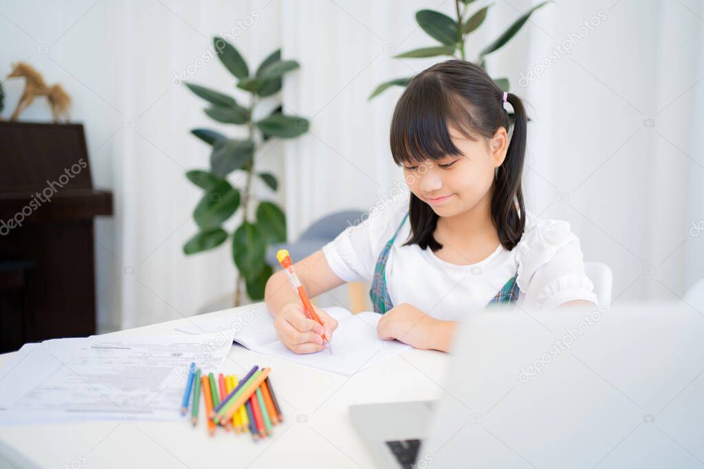 Asian girl wearing casual clothes writing a book She studied online with Zoom on her laptop at home.