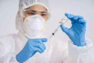 Tıbbi maske takan doktor, koronavirüsü tedavi etmek için aşı içeren bir şırınga tutuyor..