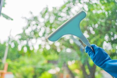 Pencereleri silmek için pencere temizleyicisi. Mavi eldiveni ver. Temizlik çubuğunu tut..