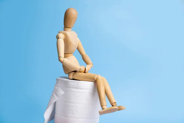 Wooden mannequin and toilet paper on light blue background. Hemorrhoid treatment.