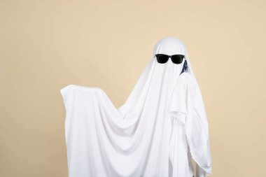 Hayalet kostümlü ve güneş gözlüklü biri telefonda bej bir arkaplanda konuşuyor. Metin için boşluk.