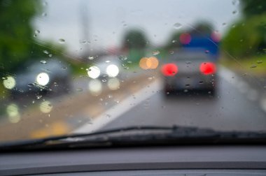 Araba yağmurda araba sürüyor. Ön camda damlalar var.