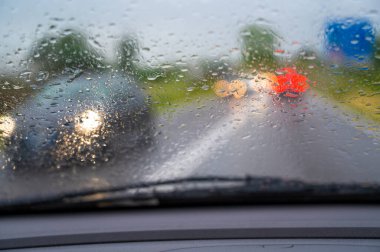 Araba yağmurda araba sürüyor. Ön camda damlalar var.