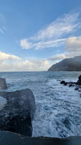 Madeira 'daki Porto da Cruz Körfezi' nde kıyı şeridi boyunca doğal deniz havuzları ve güçlü dalga hareketleriyle dalgalı bir Atlantik Denizi yer alıyor. Sahne, suyun volkanik kaya oluşumlarına karşı enerjik hareketini yakalar ve ham kıyı bölgesini vurgular.