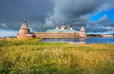 Kutsal gölün kıyısındaki Solovetsky Manastırı ve sonbahar güneşinin ışınlarında çiçekli bir çayır.