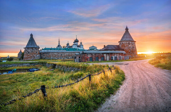 Solovetsky Monastery on the Solovetsky Islands in the light of the dawn sun and a chain fence by the road