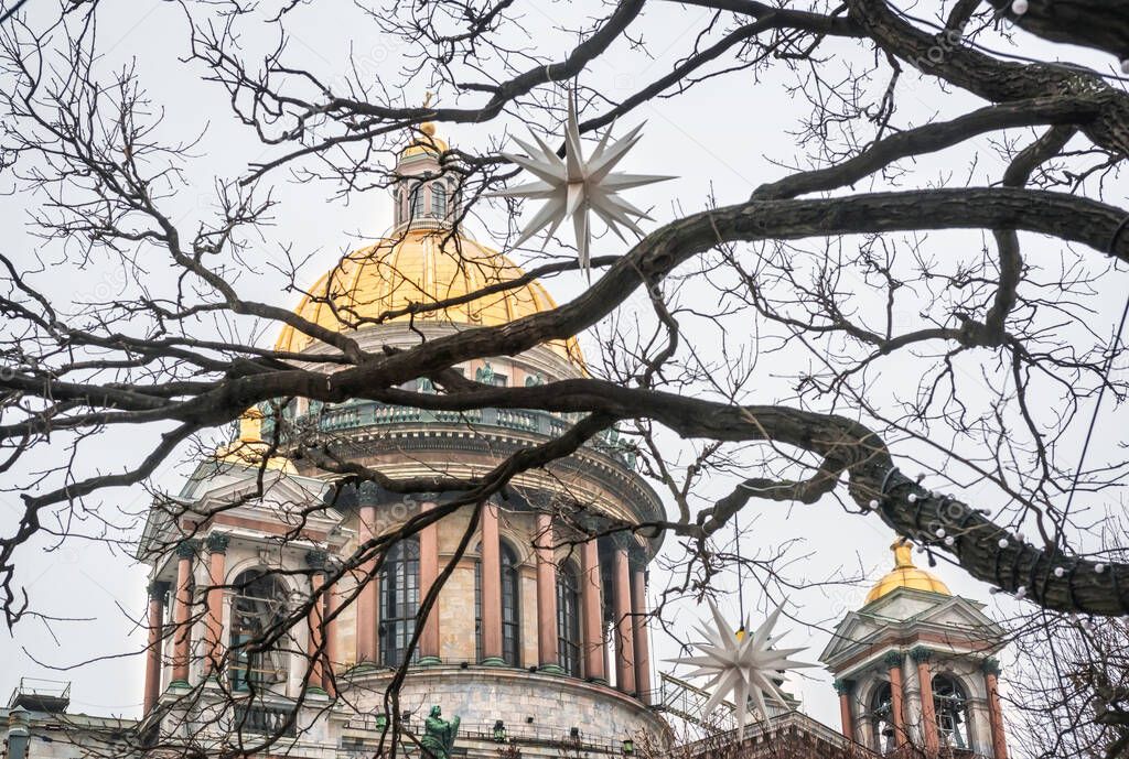 The dome of St. Isaac's Cathedral in St. Petersburg through tree branches and Christmas decorations in the form of stars under the winter sk