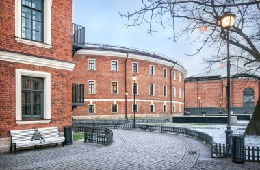 St. Petersburg 'da New Holland' ın tuğla binası ve bulutlu bir kış günü beyaz bir bank.