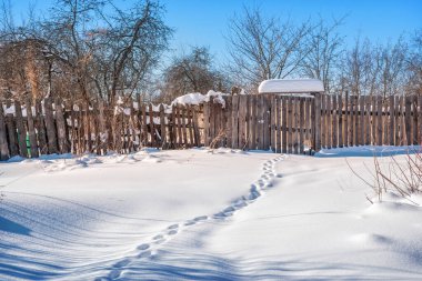 Muro 'da kış güneşli bir günde çitin içinde bir kapı ve karda ayak izleri.