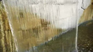 A stream of water falls on a granite stone. A lot of spray scattering in different directions.