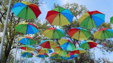 Colorful umbrellas, the colors of the rainbow, suspended against the background of a blue sky. Festive atmosphere on the city street.