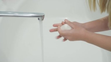 Kız ellerini özenle sabunla yıkar. Beyaz bir arkaplana karşı sığ bir alan derinliğinde yakın plan. Hijyen ve viral enfeksiyona karşı koruma.