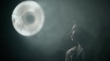 Karanlık, dumanlı bir odada, spot ışıklarıyla aydınlatılmış genç bir adam. Dramatik gece hayatı atmosferi.