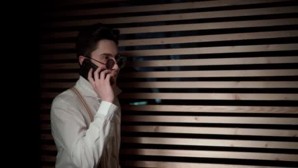 Молодой Человек Солнечных Очках Говорит Телефону Стоит Темной Комнате Рядом — стоковое видео