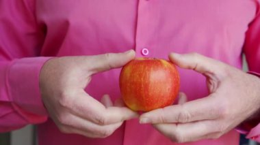 Erkek ellerinin olgun sulu bir elmayı tuttuğu yakın plan. Elmanın bir kısmını ayır.