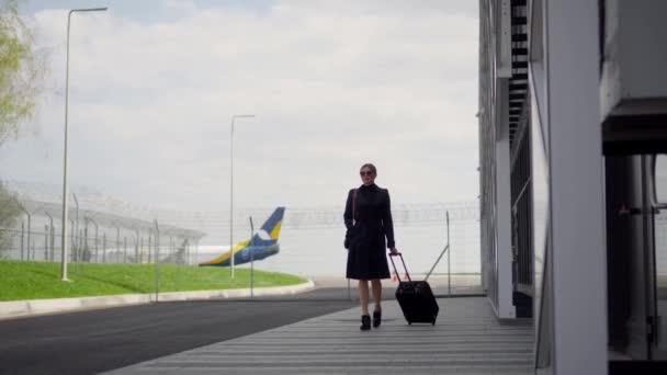 那位女商人在飞机到达后离开了机场 她把行李卷起来了 在背景下 视线不集中 离开的飞机的尾端清晰可见 — 图库视频影像