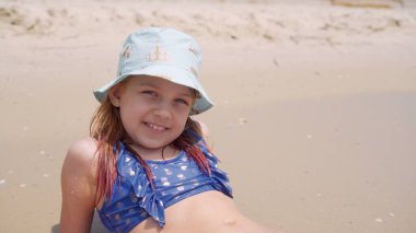 Genç bir kız sahilde güneşlenir, güneşin sıcacık ışınlarından zevk alır, kumların üzerinde uzanır..