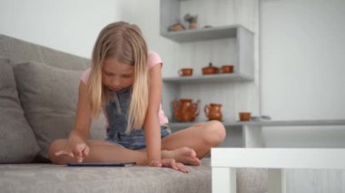 Kız evde, kanepede oturuyor ve heyecanla tableti kullanıyor..