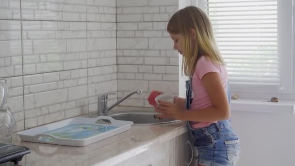 一个学龄的女孩在家里厨房里洗碗 帮助父母 — 图库视频影像