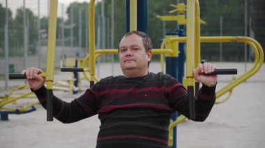 Şişman bir adam açık hava spor sahasında spor yaparak kilo vermeye çalışıyor..