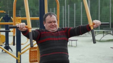 Şişman bir adam açık hava spor sahasında spor yaparak kilo vermeye çalışıyor..