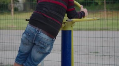 Şişman bir adam açık hava spor sahasında spor yaparak kilo vermeye çalışıyor..