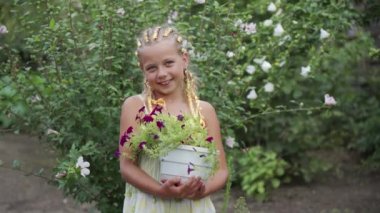 Olumlu gülümseyen okul çağındaki bir kız bahçesinde büyüyen güzel çiçekleri elinde tutuyor. Çocukça bir gülümseme. Çocuk bahçıvanlıkla meşgul..