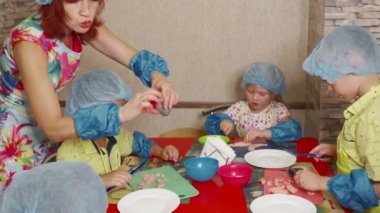 Bir grup anaokulu çocuğu, bir öğretmenin rehberliğinde, mutfakta ebeveynlere yemek pişirmede yardım etmeyi öğrenirler. Küçük çocuklar için ilkokul.