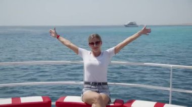 Kaygısız bir kız bir deniz gemisinde ya da yatta dinleniyor. Gülümsüyor ve zevkle ellerini kaldırıyor. Denizde yaz tatili kavramı.