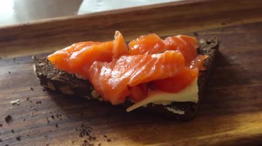 Tahtada servis edilen tereyağlı ve kırmızı balıklı bir dilim siyah ekmek..