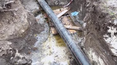 Büyük bir boru kazılmış bir hendeğe sızıyor, dibini kirli suyla dolduruyor..