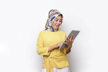 Kadın tesettür elbisesi kullanarak tablete bakıyor. Genç bir kadın dijital tabletten dışarı bakarken beyaz tablette tek başına duruyor.