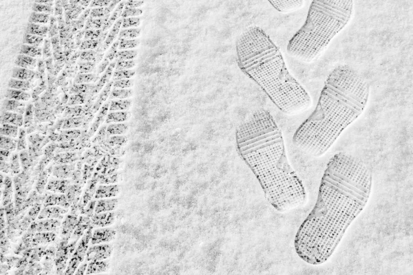 rhythmic footprint, boot tracks and car tires on thin white snow in winter go into the distance, horizontal frame, ribbed tread, winter concept
