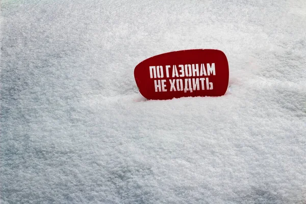 Red notice board on white snow with text in Russian do not walk on the lawns, funny inscription, joke