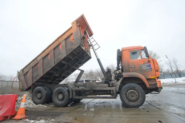 Orange dump truck KAMAZ pours snow in negotable on snow-melting point, Moscow — Stock Photo, Image