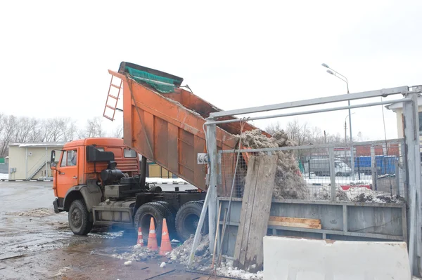 Unloading the dirty snow of the body orange truck in negotable on snow-melting point — Stock Photo, Image