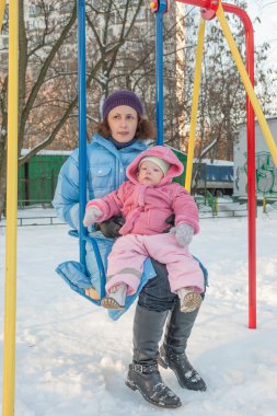 Bir kadın bir salıncakta sallanan küçük bir çocuk ile kış
