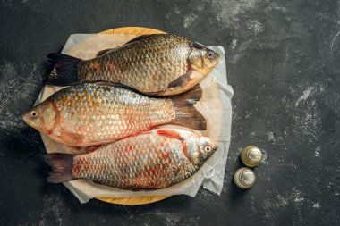tuz ve karabiber ve kopya alanı ile ahşap kesme tahtası koyu arka plan üzerinde yatan üç ham sazan balıkları