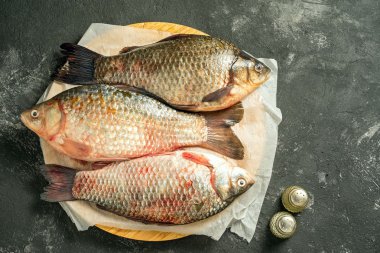 tuz ve karabiber ve kopya alanı ile ahşap kesme tahtası koyu arka plan üzerinde yatan üç ham sazan balıkları