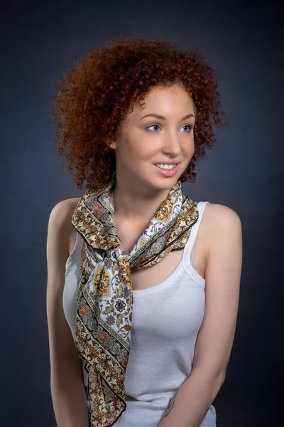 Portrait of beautiful young woman with red curly hair and blue eyes in white shirt with a scarf, studio shooting, on dark blue background — Stock Photo, Image