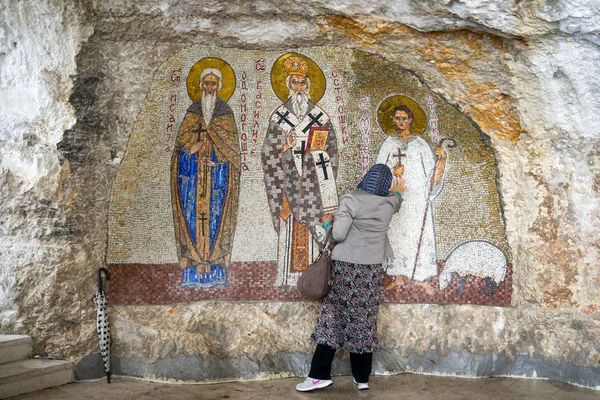 OSTROG, MONTENEGRO - 15 de maio de 2016: mulher não identificada reza nas pinturas do Muro dos Mosaicos no mosteiro ortodoxo sérvio Ostrog, Montenegro. Ostrog é o lugar de peregrinação mais popular em Montenegro . — Fotografia de Stock