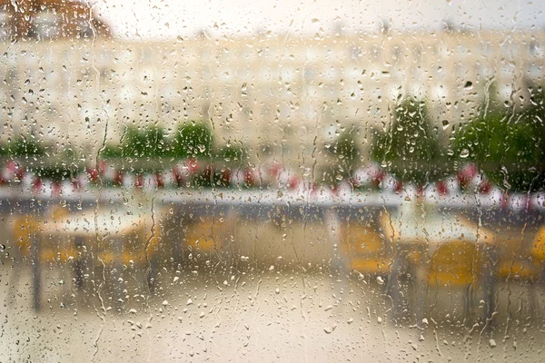 Νερό και τη βροχή που πέφτει στο γυαλί, αφηρημένη άποψη σχετικά με ένα άδειο καφετέρια και το κτίριο — Φωτογραφία Αρχείου