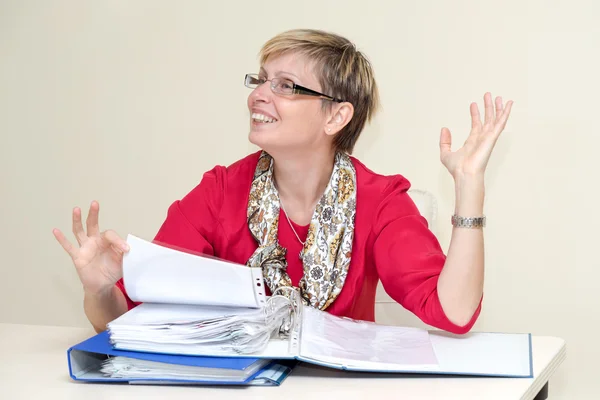 Zakenvrouw zitten door een bureau met een stapel papier, glimlachend en bedrijf in haar handen — Stockfoto