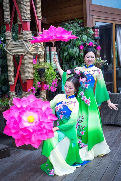 Två vackra asiatiska tjejer i traditionella kinesiska blå och gröna klänningar med paraply i form av lotusblommor — Stockfoto