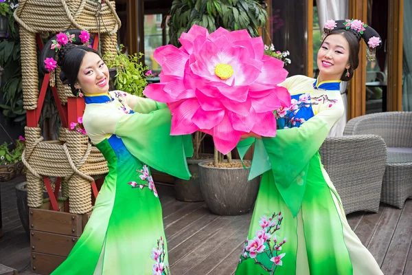Två vackra asiatiska tjejer i traditionella kinesiska blå och gröna klänningar med paraply i form av lotusblommor — Stockfoto